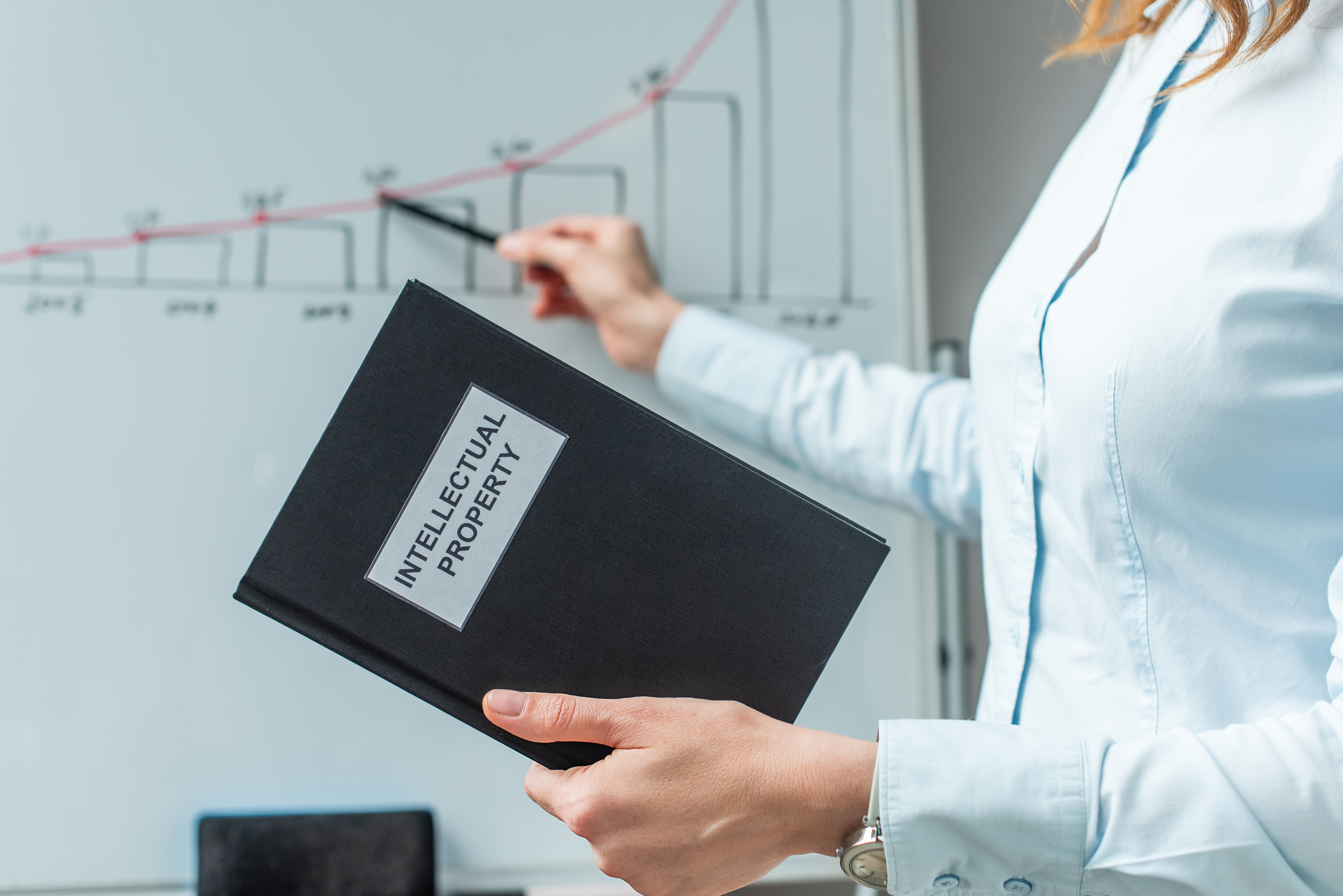 Cropped view of lawyer holding book with intellectual property lettering and pointing with pen at